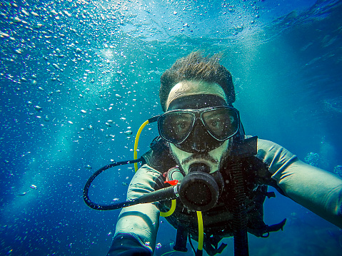 Young diver in the ocean, taking a selfie with blue water background.