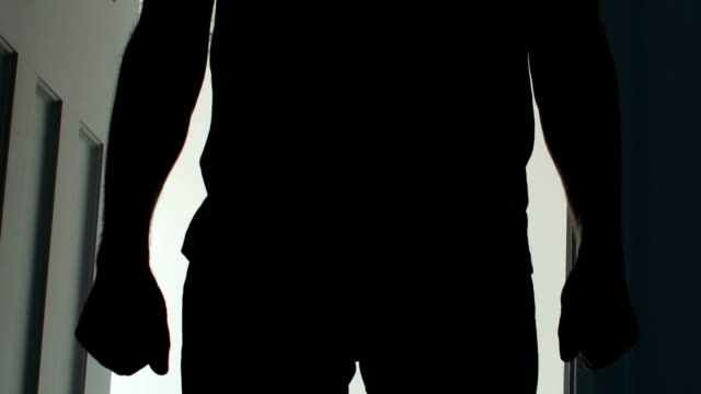 Silhouette of a man opening a door and entering a dark room.
