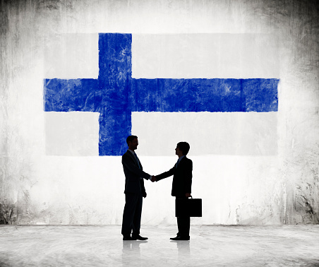 Two Businessmen Shaking Hands With Finnish Flag As A Background