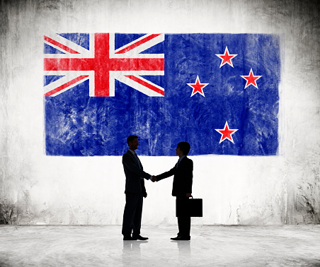 Two Businessmen Shaking Hands With New Zealander Flag As A Background