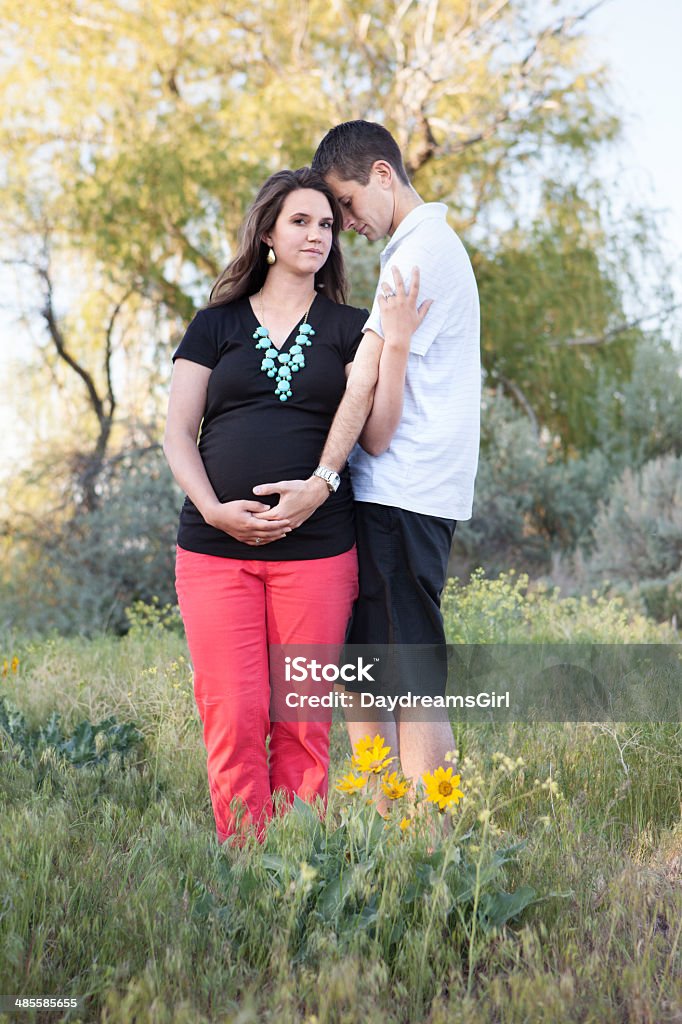 Husband and Pregnant Wife Outdoors in Widlflowers Husband and pregnant wife outdoors standing in meadow of wildflowers. Adult Stock Photo