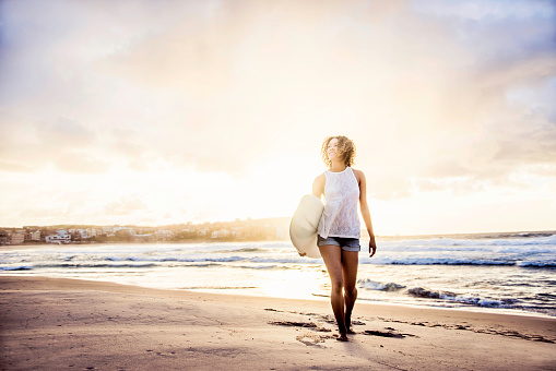 Happy female surfer walking at the beach with a surfboard