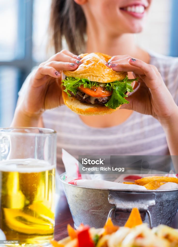 Young Woman and Burger A young woman eating a burger in a restaurant. Eating Stock Photo