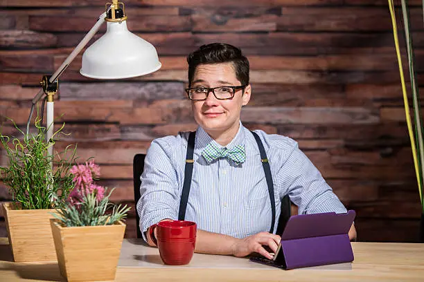 Flattered dapper woman with bowtie at desk with a red coffee cup