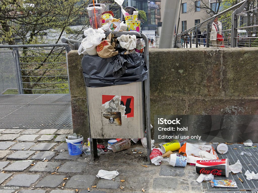 crowded garbage can Nuremberg, Germany - March 31, 2014: crowded garbage can with paper, plastic and many widespread  fast food packages on the ground. Garbage Can Stock Photo