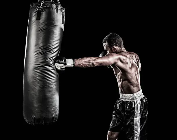 Boxer training with punching bag on black background