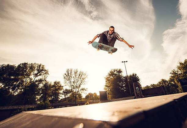 Low angle view of a young man skateboarding at sunset. Young extreme skateboarder practicing at the park against the sky. x games stock pictures, royalty-free photos & images