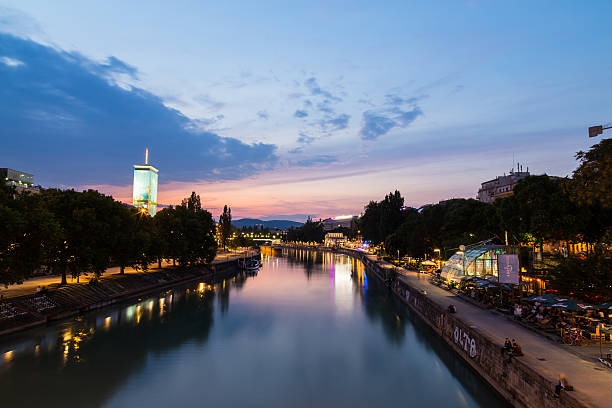 Vienna, Austria - August 21, 2015: A view along the Danube Canal shortly after sunset. People, buildings and bars can be seen.