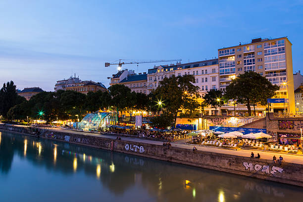Vienna, Austria - August 21, 2015: A view along the Danube Canal during the blue hour. People, buildings and bars can be seen.