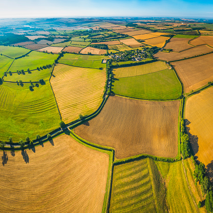 Aerial view over picturesque patchwork landscape of green pasture, lush meadows and golden wheat crop fields amongst the rolling hills and quiet valleys below blue summer skies. ProPhoto RGB profile for maximum color fidelity and gamut.