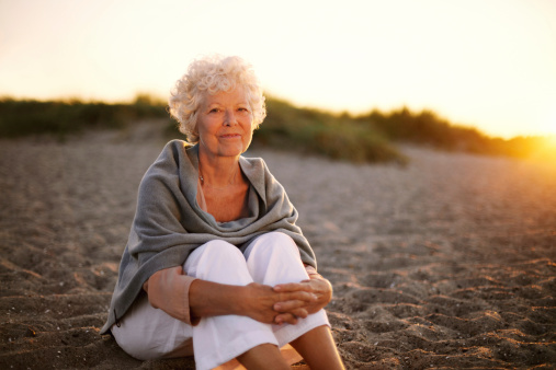 Portrait of happy old woman sitting on the beach. Retired caucasian lady relaxing outdoors