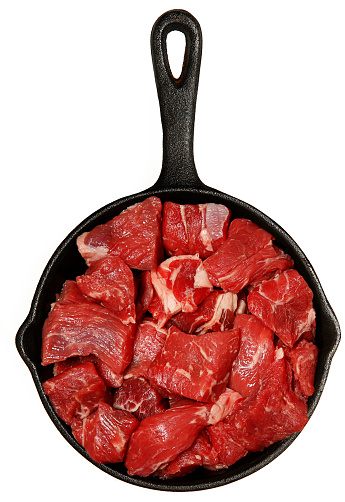 Raw Beef Cubes Chopped in Cast Iron Skillet Over White.