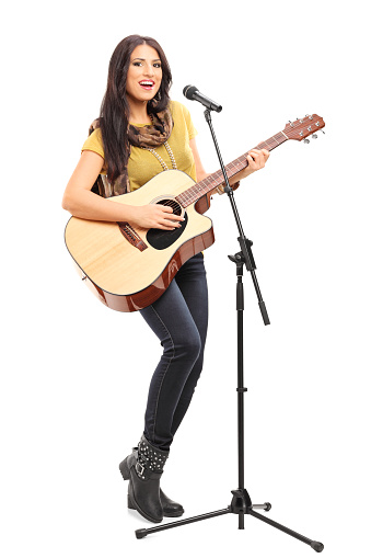 Full length portrait of a female singer playing on acoustic guitar and singing on a microphone isolated on white background