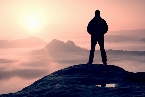 Hiker standing on top of a mountain and enjoying sunrise
