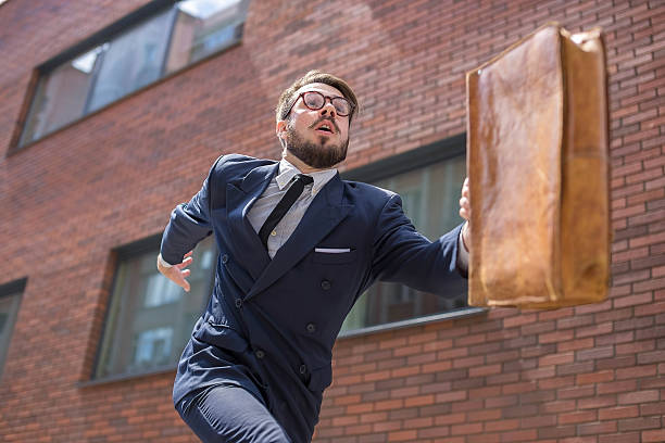 young businessman running in a city street Young businessman with a briefcase and glasses running in a city street on a background of red brick wall. concept of rapid career man rushing stock pictures, royalty-free photos & images
