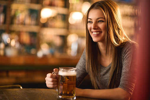Beautiful smiling young woman sitting in a pub and holding a glass of beer.