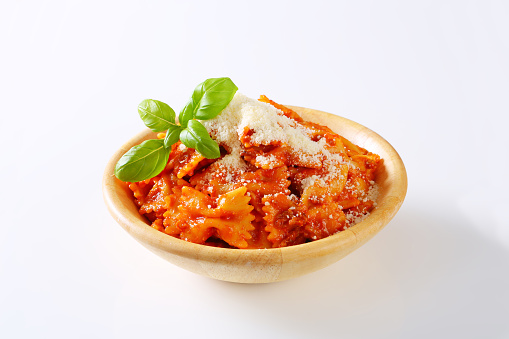 bowl of farfalle pasta with tomato sauce and grated parmesan on white background