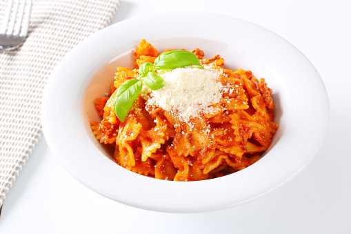 plate of farfalle pasta with tomato sauce and grated parmesan on white background