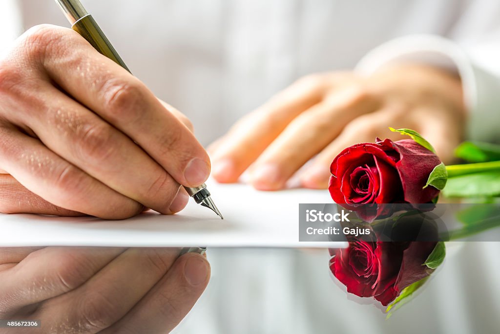 Romantic man writing a love letter Closeup of the hands of a romantic man writing a love letter to his sweetheart for Valentines Day to be accompanied by a single beautiful fresh red rose 2015 Stock Photo