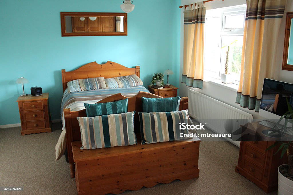 Image of colour coordinated bedroom suite with pine bed furniture Photo showing luxury bedroom suite with large double bed, pine furniture and colour coordinated turquoise furnishings, with beige carpet and a white panelled door - like a hotel room. Bedding Stock Photo