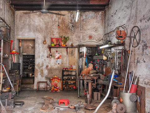 Penang, Malaysia - August 6, 2015: Mature asian man welding metal in his workshop whilst sitting.