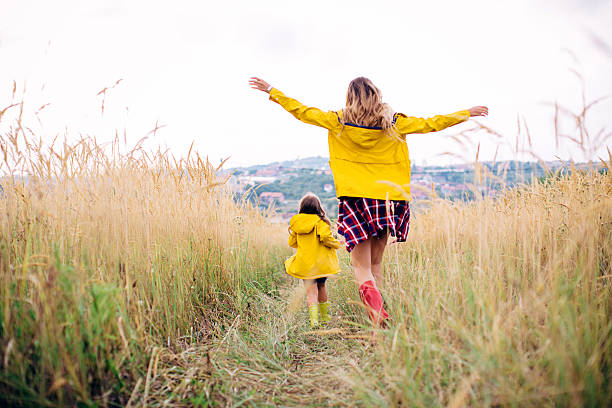 Mother with her cute daughter in meadow. Mother with her cute daughter, walking through the meadow. Autumn, yellow grass. Caucasian, blond hair. Wearing rubber boots. From behind. yellow shoes stock pictures, royalty-free photos & images
