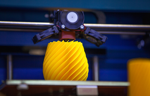 Blue three dimensional printer working creating a yellow plastic object.