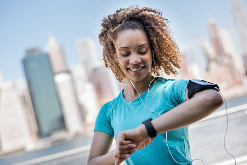 Sportive woman tracking her workout progress with a smart watch and wearing an arm band for her cell phone