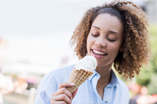 Happy African American woman eating ice cream at the park and looking happy enjoying the summer