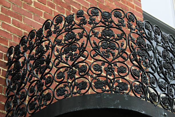 Wrought iron cemetery gate with angels on it in front of white door and bricks.