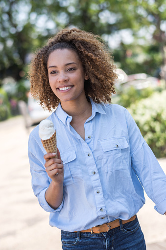 Casual woman eating ice cream at the park on a summer day and looking very happy