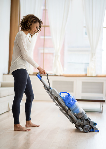 Young African American woman vacuuming her house with a vacuum and looking happy