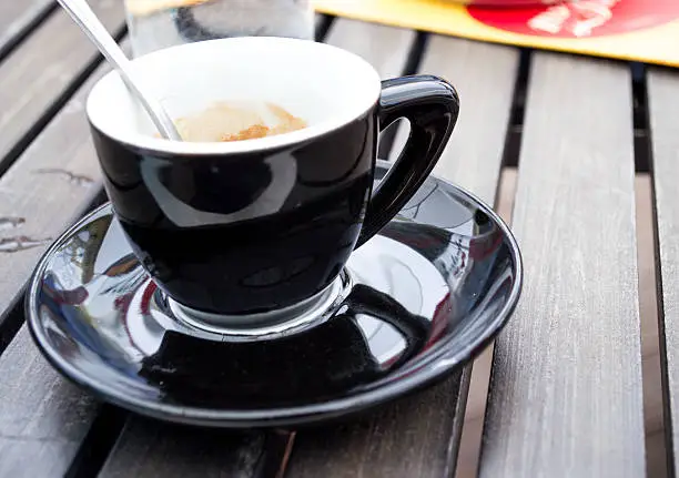 A small coffee cup, used to serve strong espresso,  on a table at a cafe.