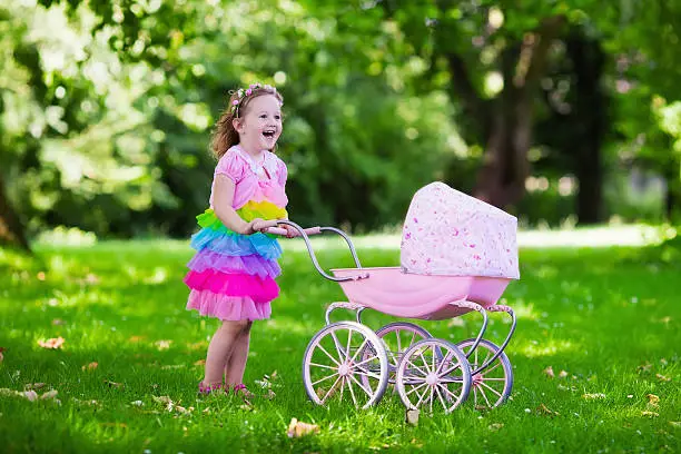 Photo of Little girl pushing a toy stroller wth doll