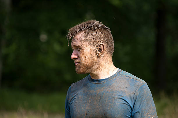 Tierd looking man with face caked in mud Сirencester, England - August 22, 2015: Man with face caked in mud looks tired on his gruelling 12 mile assault course during the ‘Tough Mudder’ challenge in Cirencester park, Gloucestershire. This annual event is a team-based 10-12 mile obstacle course designed to test physical strength endurance. tierd stock pictures, royalty-free photos & images