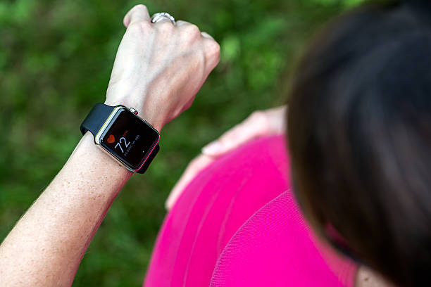 Pregnant Woman Taking Pulse on Apple Watch Laval, Canada - August 25, 2015: A pregnant woman wearing and using a 42mm 316L Stainless Steel Apple Watch to check her heart rate. The Apple Watch became available April 24, 2015 and is the latest device produced by Apple. cardiac conduction system stock pictures, royalty-free photos & images