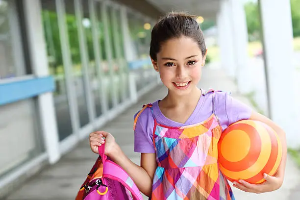 Smiling girl holding a ball and backpack