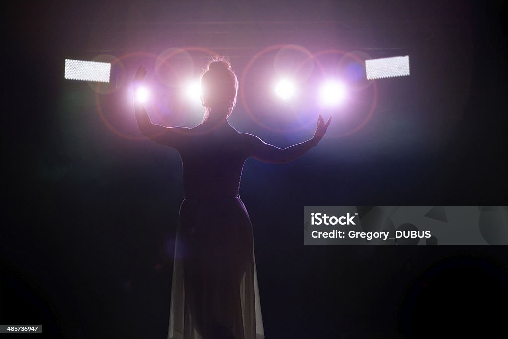 Artist saluting the public Young women artist (singer or classical dancer) is saluting the public. Rear view from backstage with spotlight in camera lense. Opera Stock Photo