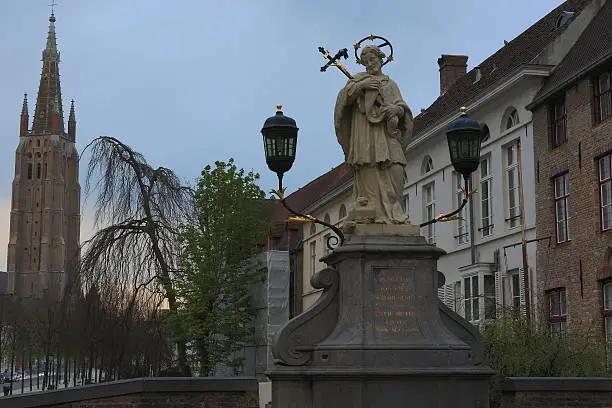 Bruges - The tower of church of Our Lady and st. John the Nepomuk statue on the bridge.