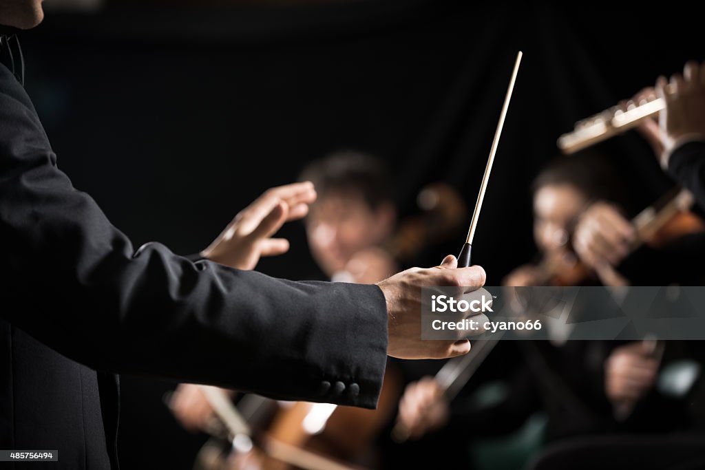 Orchestra conductor on stage Conductor directing symphony orchestra with performers on background, hands close-up. Orchestra Stock Photo