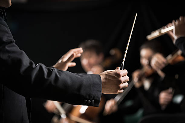 Orchestra conductor on stage Conductor directing symphony orchestra with performers on background, hands close-up. musical conductor stock pictures, royalty-free photos & images