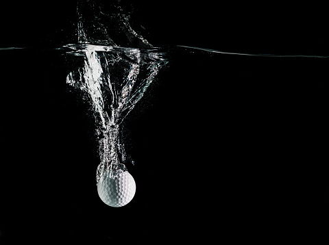 A close up of a golf ball splashing in water on a black back ground.  http://blog.michaelsvoboda.com/GolfBanner.jpg