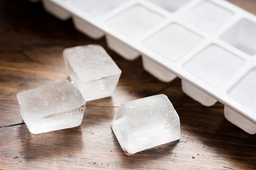 Ice cube tray filled with ice cubes and three lose ice cubes against dark wood.