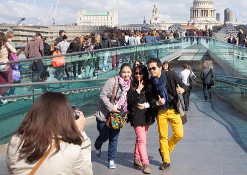 London, England - April 18, 2014: Three young Asian tourists pose for a photo on the Millennium Bridge in front of St Paul's Cathedral in London.