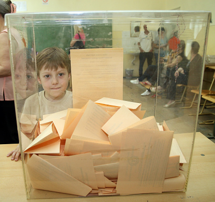 The boy looks at the ballot paper in the ballot box in elections