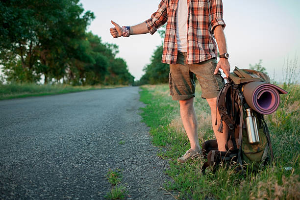 Young smilimg caucasian tourist hitchhiking along a road Young smilimg caucasian tourist with backpack hitchhiking along a road in sunset hitchhiking stock pictures, royalty-free photos & images