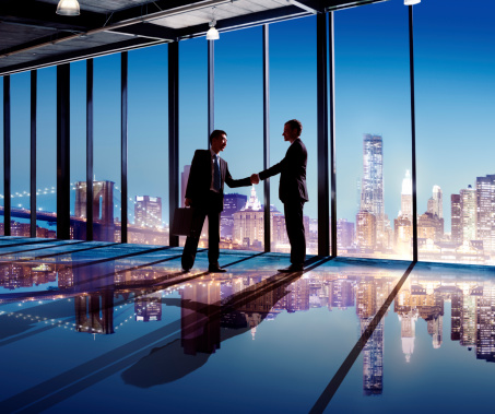 Multi-Ethnic Businessmen Shaking Hands Indoors With City As A Background