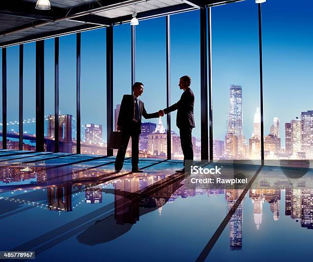Multiethnic Businessmen Shaking Hands Indoors With City As A Background Stock Photo - Download Image Now