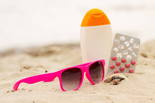 Pink sunglasses, shells, sun lotion and pills of vitamin E on sand at the beach, seasonal concept and successful tanning