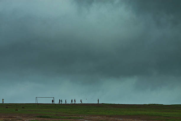 Kids playing football on flat plain with overcast sky. This is a monsoon season and still kids play football in rain; this is the charm of childhood. In this picture tried to capture the kids playing football and sky is overcast and almost about to rain.